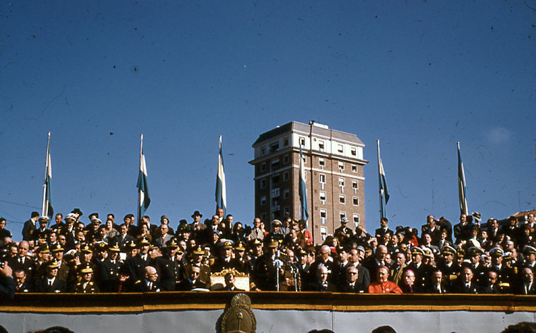 Palco de autoridades con banderas y escudo nacional durante el acto.